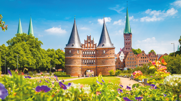 Holstentor in Lübeck vor sommerlicher Kulisse mit Blumen im Vordergrund.